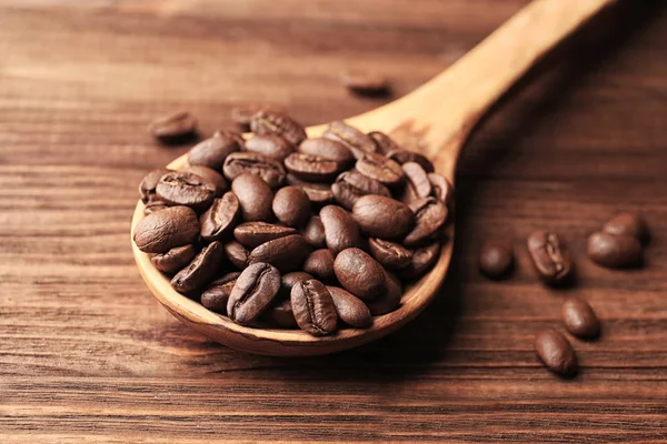 Cucchiaio di legno e chicchi di caffè su sfondo di legno, vista da vicino — Foto Stock