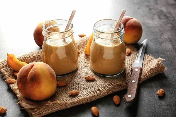 Mason jars med smoothie, persikor och servett på grå bord — Stockfoto