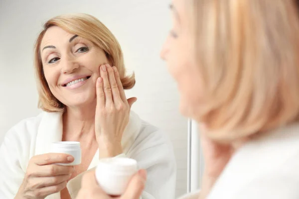 Mujer mayor aplicando crema cosmética — Foto de Stock