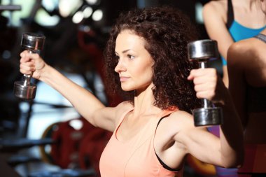 Spor salonunda dambıllarla antrenman yapan genç bir kadın.