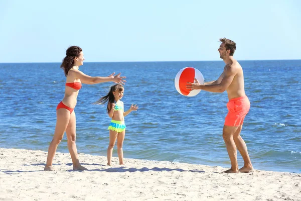 Concepto familiar. Los padres y la hija jugando con la pelota en la playa — Foto de Stock