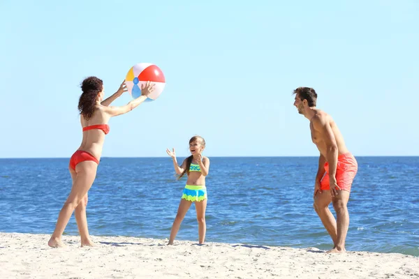 Concepto familiar. Los padres y la hija jugando con la pelota en la playa — Foto de Stock