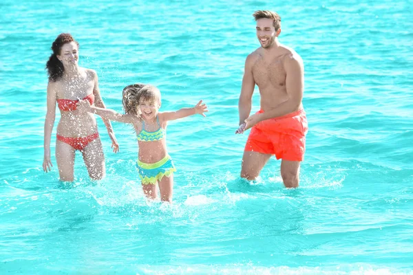 Cheerful parents playing with little girl in water