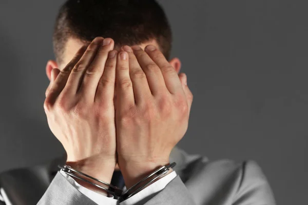 Человек в наручниках прячет лицо на сером фоне — стоковое фото