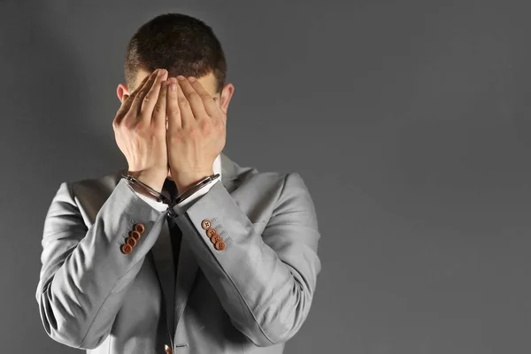 Mann in Handschellen versteckt Gesicht auf grauem Hintergrund — Stockfoto