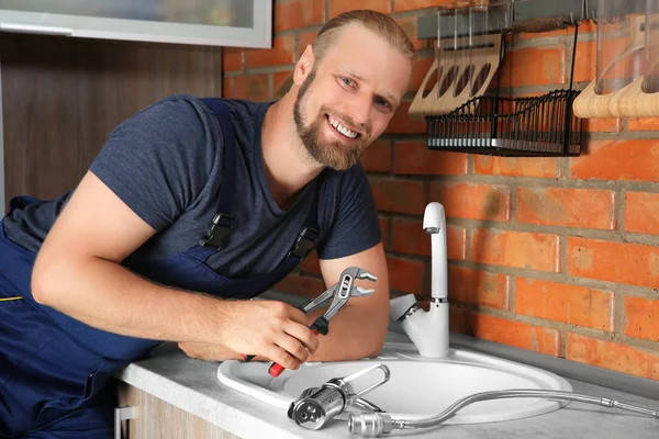 Handsome plumber replacing faucet in kitchen, close up view — Stock Photo, Image