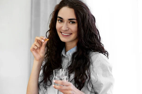 Portrait of young woman with fish oil capsule and glass of water, on light background