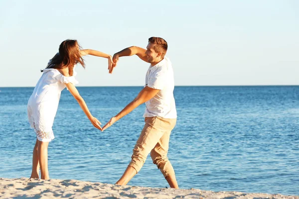 Joven pareja haciendo corazón con sus manos en la playa —  Fotos de Stock