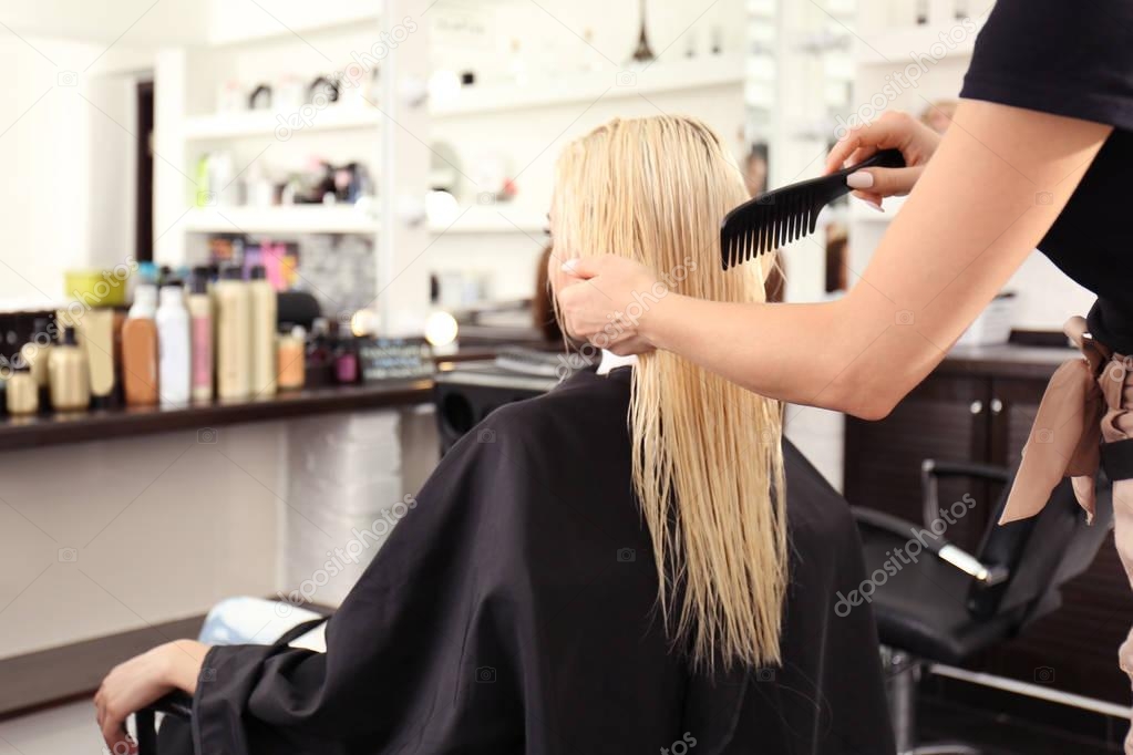 Hairdresser combing blonde's hair at salon