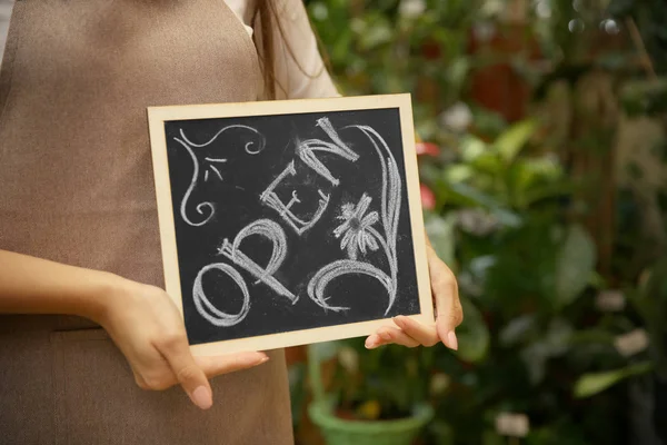Young florist holding board with inscription OPEN