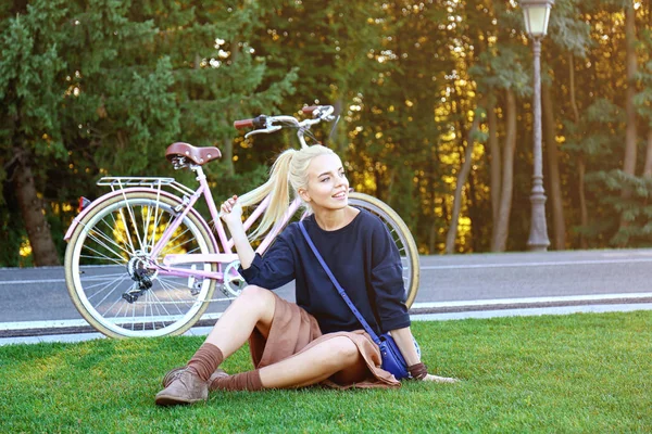 Vrouw zitten op gazon in de buurt van fiets — Stockfoto