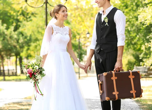 Sposo e sposa con valigia vintage passeggiando nel parco — Foto Stock