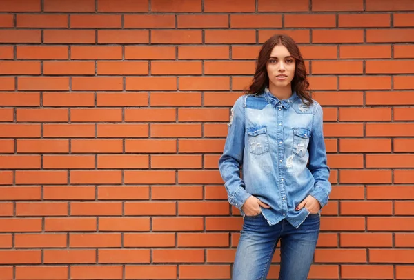 Young woman in casual clothes standing against brick wall — Stock Photo, Image