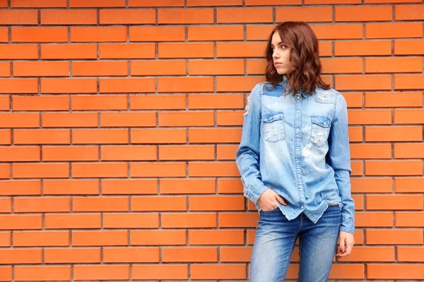 Young woman in casual clothes standing against brick wall — Stock Photo, Image