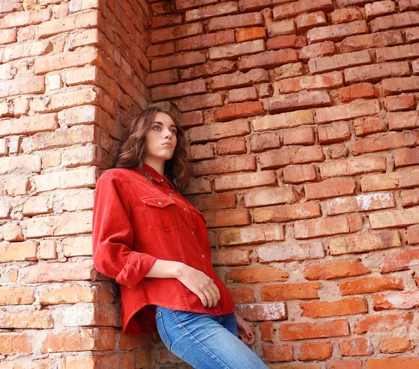 Pretty young woman leaning against brick wall — Stock Photo, Image
