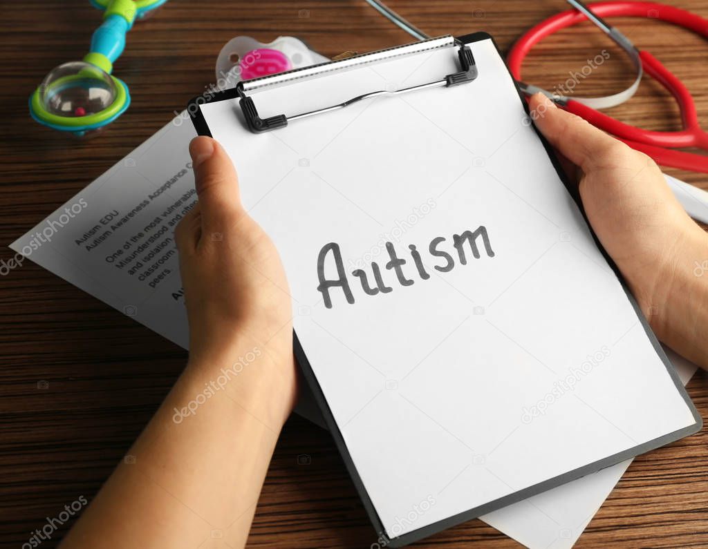 hands holding paper with word AUTISM