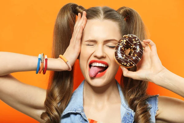 Забавная молодая женщина с вкусным пончиком на оранжевом фоне, закрыть — стоковое фото