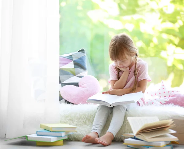 Little girl with book sitting on windowsill — Stock Photo, Image