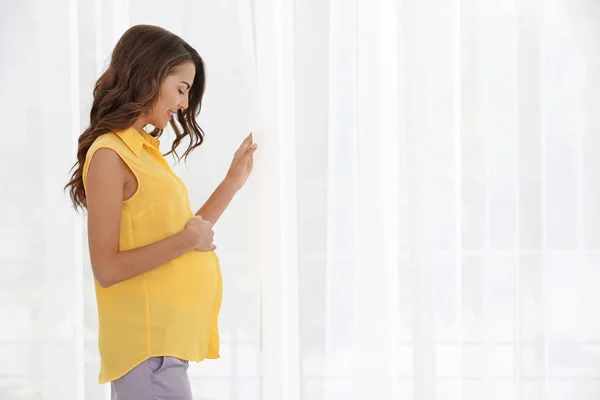 Zwangere vrouw staat in de buurt van raam thuis — Stockfoto