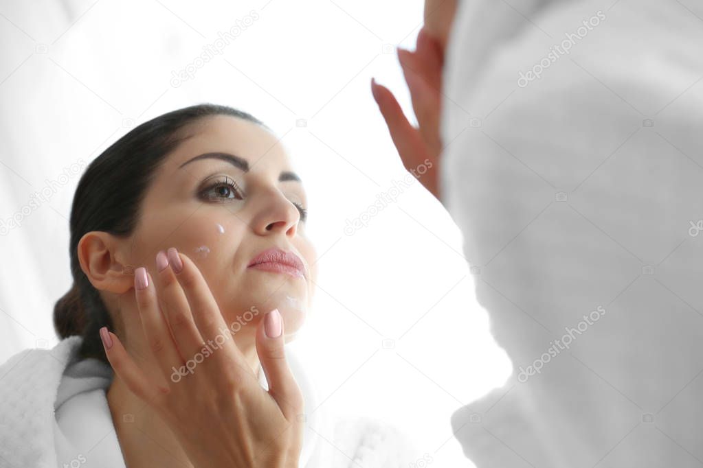 Adult woman applying cream on face in mirror reflection