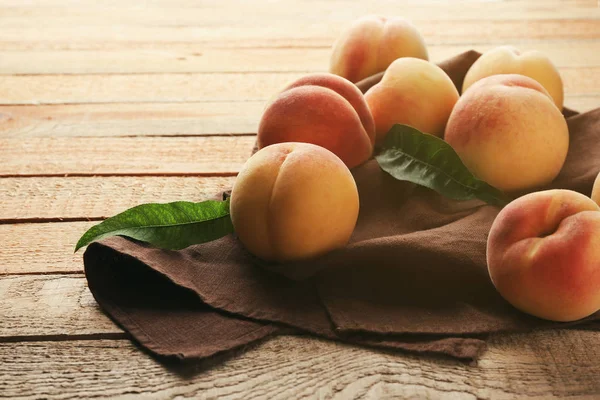 Fresh juicy peaches on brown napkin and wooden background — Stock Photo, Image