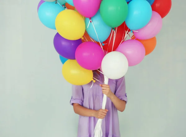 Menina segurando muitos balões coloridos no fundo da parede — Fotografia de Stock