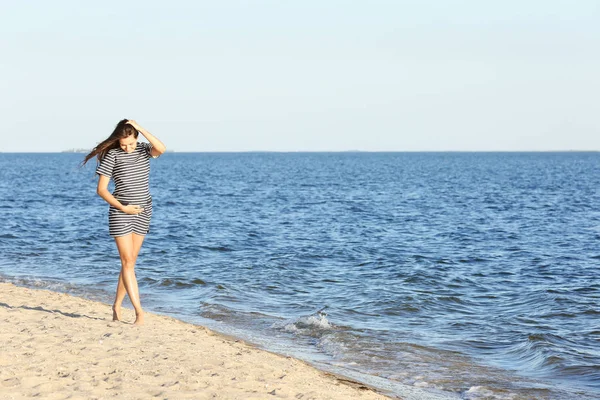 Beautiful pregnant woman in striped dress walking on the beach — Stock Photo, Image