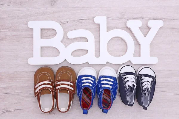 Différentes chaussures de bébé et mot BABY sur le sol en bois, vue de dessus — Photo