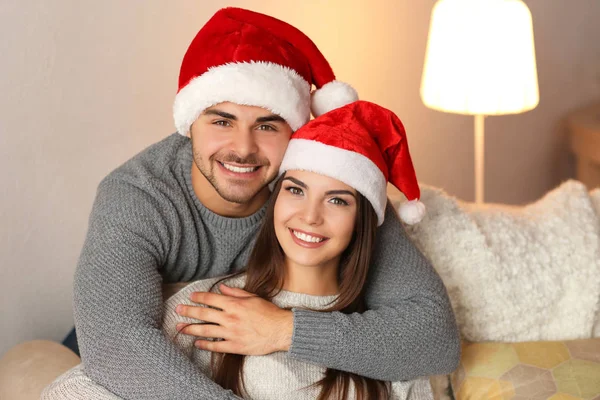 Молодая пара в шляпах Санта-Клауса отдыхает дома — стоковое фото