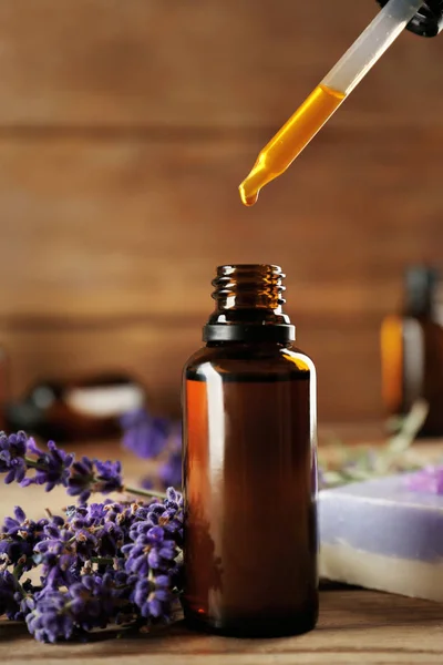 Pipette dropping essential oil into a glass bottle on wooden background — Stock Photo, Image