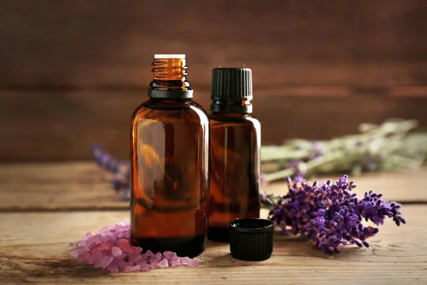 Bottle with aroma oil, sea salt and lavender flowers on wooden background — Stock Photo, Image