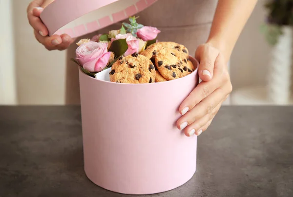 Vrouwelijke bloemist voorbereiding doos met prachtige bloemen en koekjes, close-up — Stockfoto