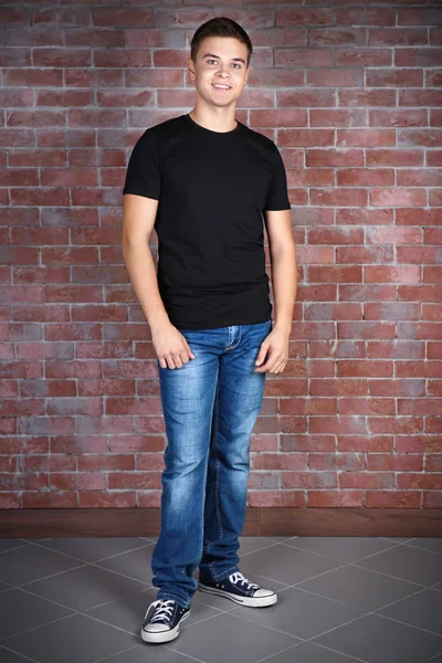 Handsome young man in blank black t-shirt standing against brick wall — Stock Photo, Image