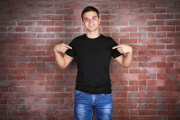 Przystojny, młody człowiek w puste czarny t-shirt stoi mur z cegły — Zdjęcie stockowe