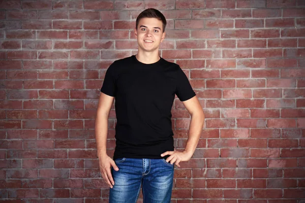 英俊的年轻男子，在空白的黑色 t 恤站对抗墙面砖 — 图库照片