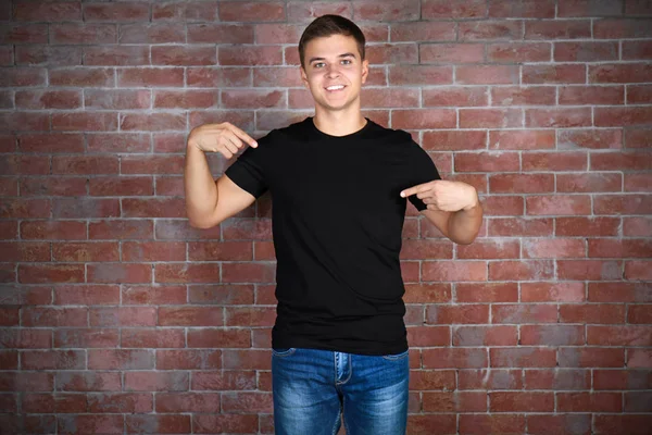 Schöner junger Mann in schwarzem T-Shirt steht vor Ziegelmauer — Stockfoto