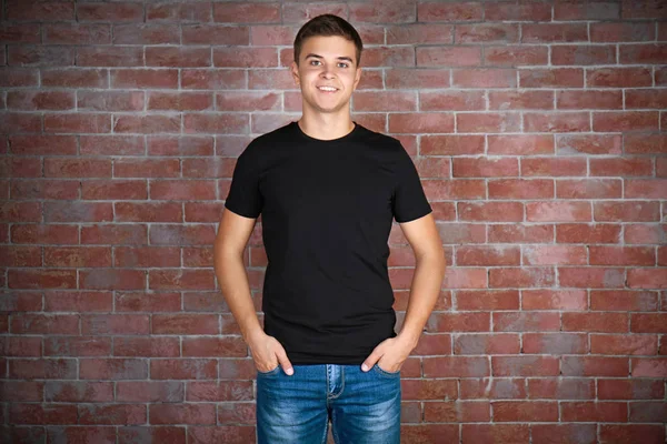 英俊的年轻男子，在空白的黑色 t 恤站对抗墙面砖 — 图库照片