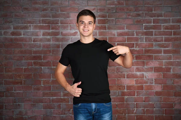 Bello giovane uomo in bianco nero t-shirt in piedi contro muro di mattoni — Foto Stock