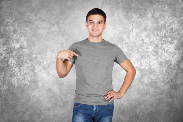 Όμορφος νεαρός άνδρας στο κενό γκρι t-shirt στέκεται ενάντια στην υφή τοίχο — Φωτογραφία Αρχείου