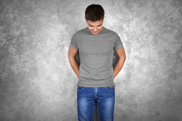 Pohledný mladý muž v prázdné šedé tričko stojící zdi texturou — Stock fotografie