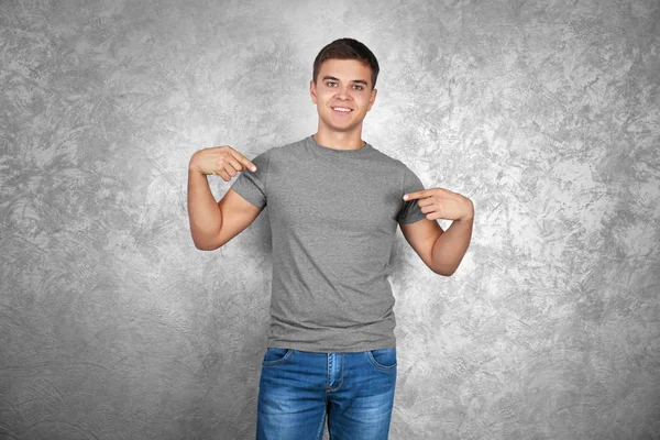 Schöner junger Mann in leerem grauen T-Shirt steht vor strukturierter Wand — Stockfoto