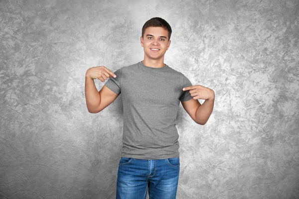 Handsome young man in blank grey t-shirt standing against textured wall — Stock Photo, Image