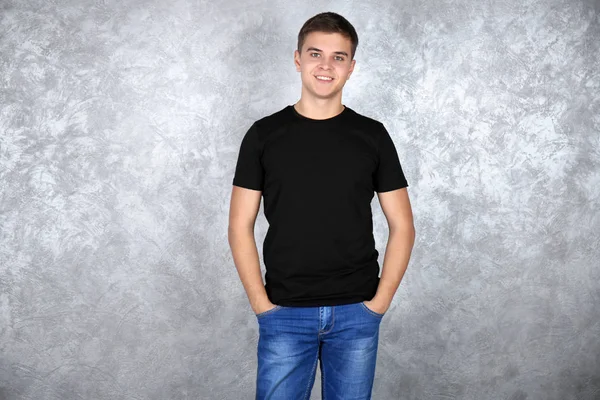 Beau jeune homme en t-shirt blanc noir debout contre un mur texturé gris — Photo