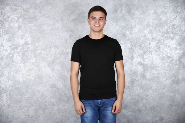 Stilig ung man i blank svart t-shirt stående mot grå texturerat vägg — Stockfoto