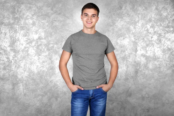 Beau jeune homme en t-shirt blanc gris debout contre un mur texturé — Photo