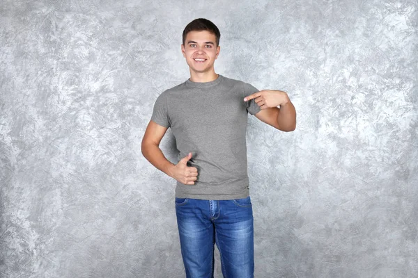 Красивый молодой человек в пустой серой футболке стоит напротив текстурированной стены — стоковое фото