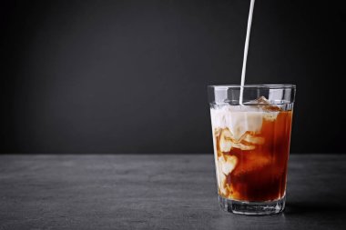 Buzlu kahvenin içine gri arka planda süt dökmek