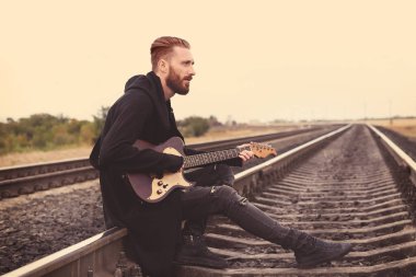 Yakışıklı adam demiryolu üzerinde gitar çalmak