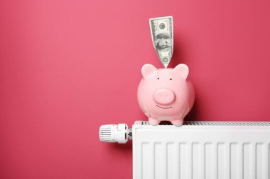 Tasarruf kavramı. Kumbara ve pembe bir arka plan üzerinde sıcaklık regülatörü ile radyatör Isıtma para