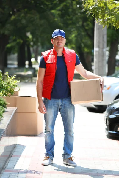 Jovem entregador masculino com caixa ao ar livre — Fotografia de Stock